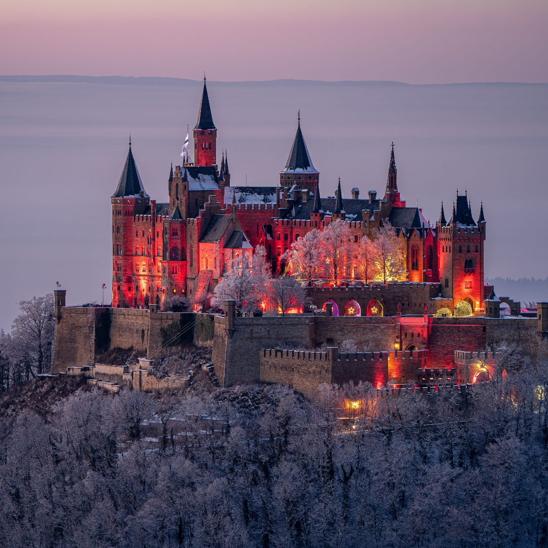 Foto der orangerot beleuchteten Burg Hohenzollern bei D&auml;mmerung