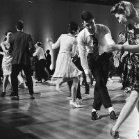 Mehrere Paare tanzen Lindy Hop in einem Saal mit Holzboden