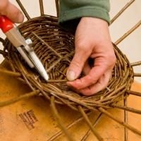 Zwei H&auml;nde mit roter Zange, die den Boden eines Weidenkorbes bearbeiten