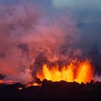Foto eines Vulkanausbruches in der D&auml;mmerung und einer beleuchteten Burg

