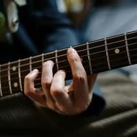 Nahaufnahme einer Hand, die auf dem Griffbrett einer Gitarre Akkorde greift