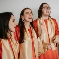 Gruppe von vier singenden Personen in orangen Gew&auml;ndern mit goldfarbenen Schals