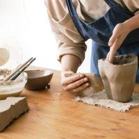 Person formt mit beiden H&auml;nden ein Gef&auml;&szlig; aus Ton auf einem Holztisch