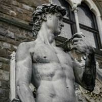 Marmorskulptur eines muskul&ouml;sen nackten Mannes mit erhobenem Arm vor einem historischen Geb&auml;ude