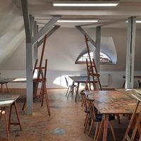 Atelier mit Holzbalken, Staffeleien, Tischen und St&uuml;hlen unter einem Dach mit Dachfenstern
