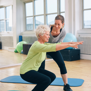 Eine Gymnastiktrainerin hilft einer älteren Dame bei einer Rückenübunng