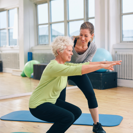 Eine Gymnastiktrainerin hilft einer älteren Dame bei einer Rückenübunng