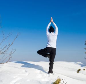 Eine Frau die im Schnee auf einer Bergspitze eine Yogaübung macht